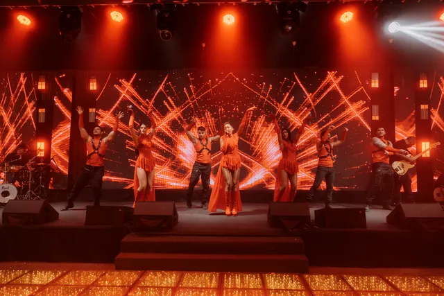 Palco inteiro aceso em vermelho, com feixes de luz e todo o grupo em cena