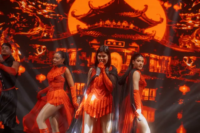 Três artistas de vermelho cantam e dançam diante do cenário oriental em LED